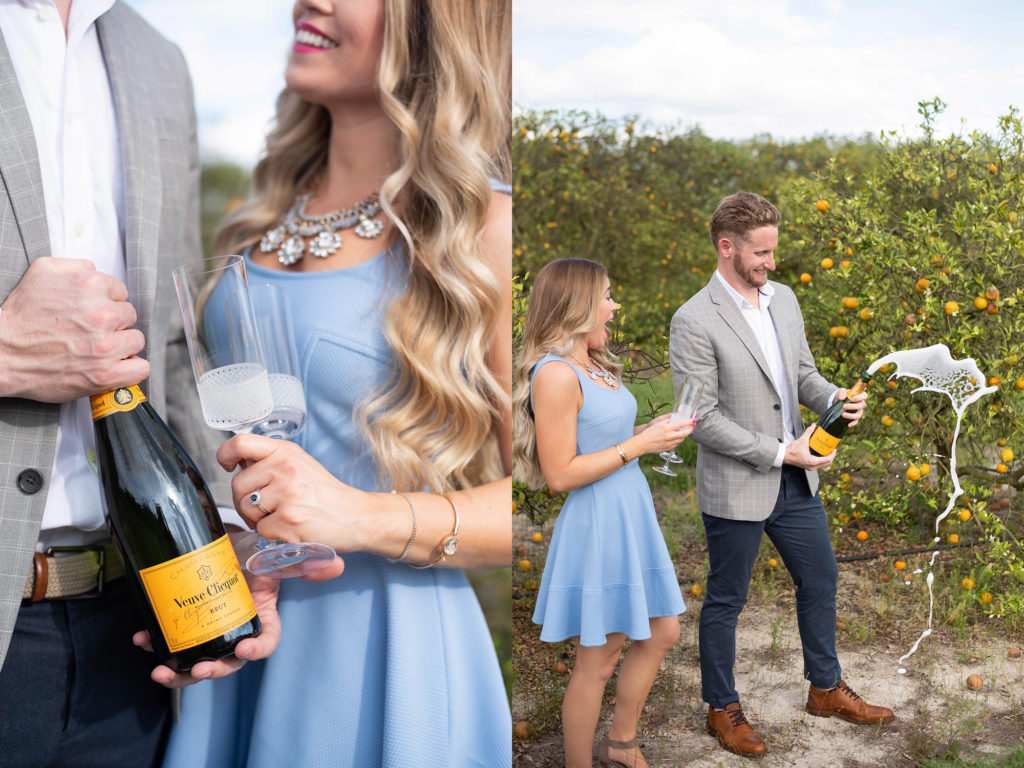 Hancock Orange Groves Engagement Session Couple wearing short blue dress and gray blazer popping champagne and smiling