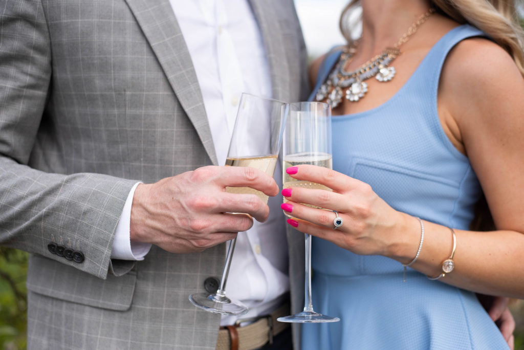 Hancock Orange Groves Engagement Session Woman wearing a light blue dress and silver blue engagement ring man wearing a gray blazer and white shirt holding champagne glasses