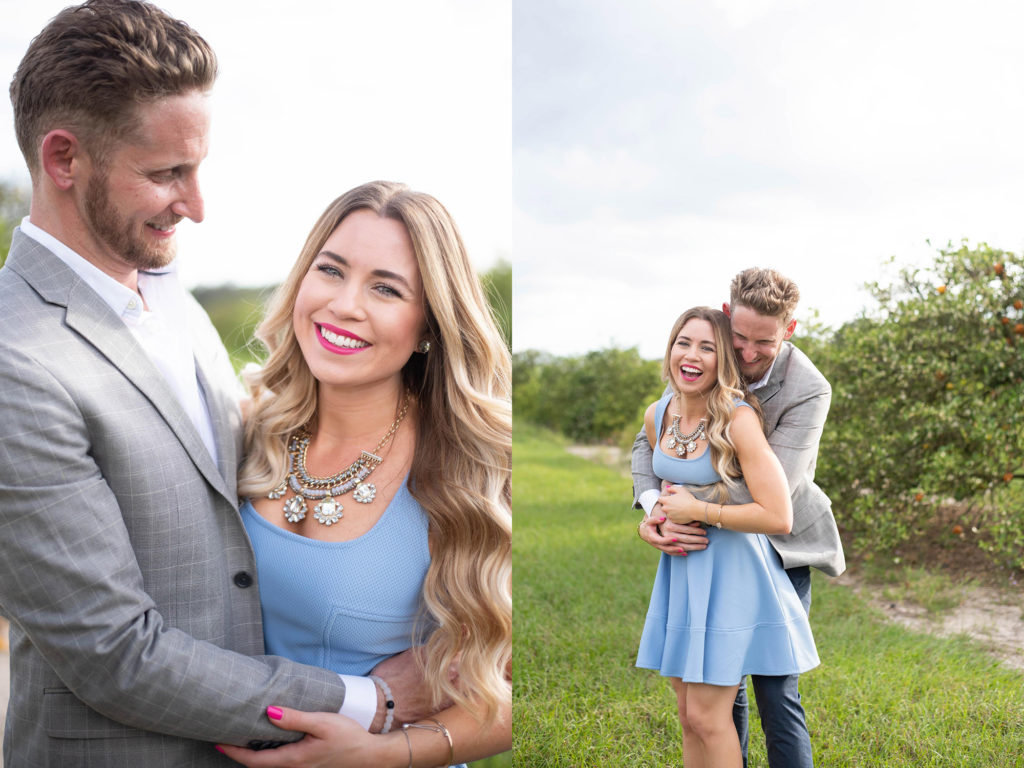 Hancock Orange Groves Engagament Session Playful couple woman looking at camera wearing short blue dress and man wearing grey blazer 