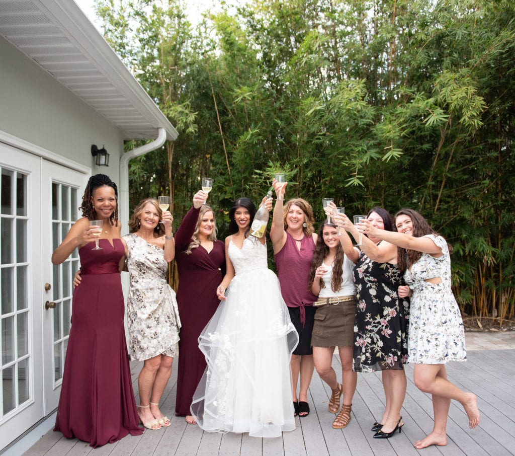 Ybor City Museum Garden Wedding Bride holding champagne bottle and bridesmaids holding champagne glasses and wearing burgundy dresses all toasting in excitement