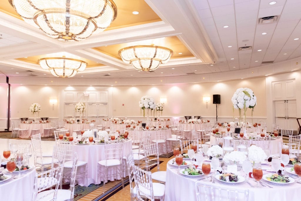marriott grand ballroom wedding in tampa airport decor in blush and silver reception tables clear chairs and vases with draping flowers
