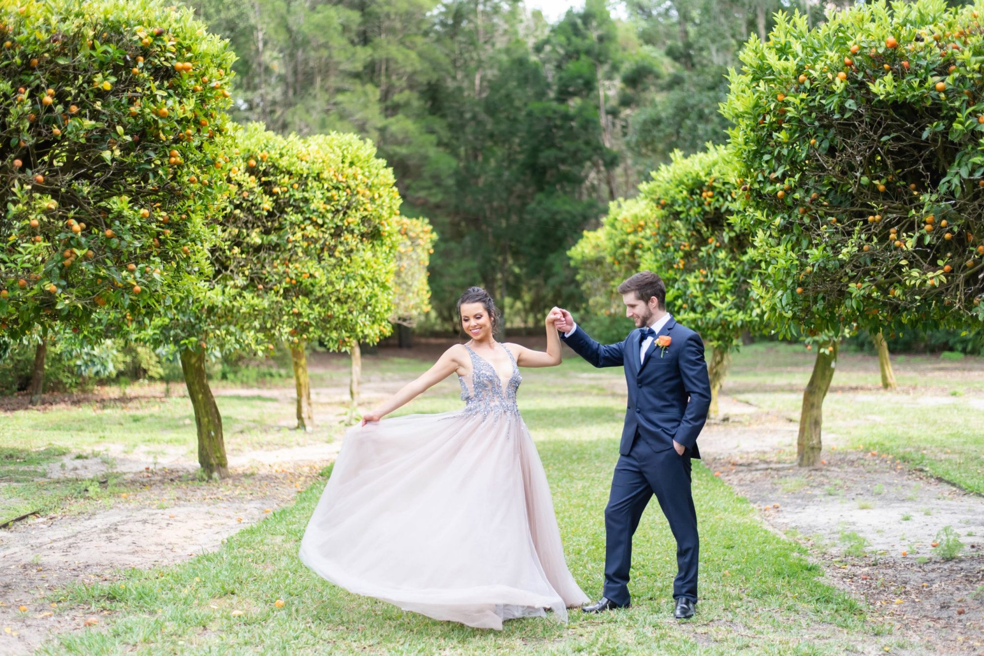 Bok tower gardens citrus wedding bride in pink blush gown spinning groom in navy tuxedo holding her in orange grove