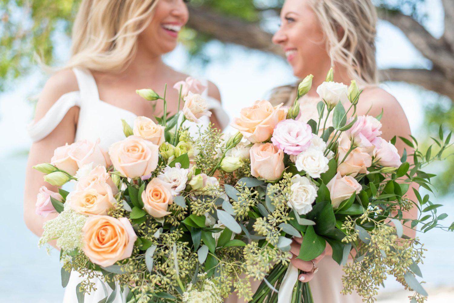 Key west marriott beachside wedding bride and bridesmaid by the beach laughing smiling at each other holding colorful pastel wedding flower bouquets
