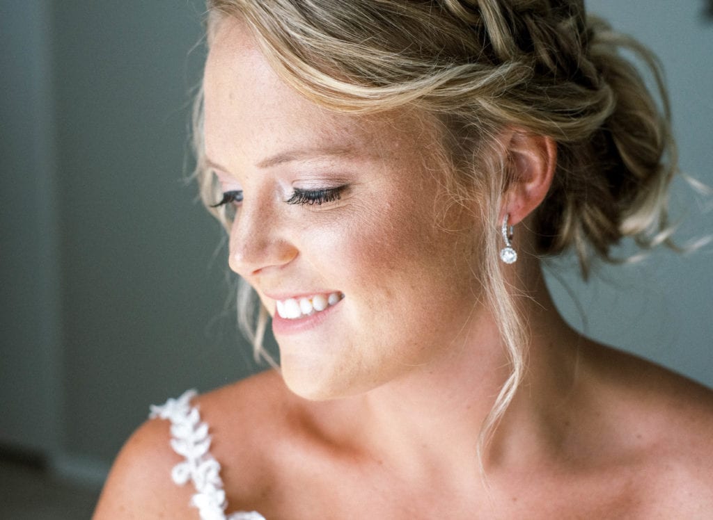 Tampa bride photo in wedding dress by Rebecca Ingram wearing diamond earrings and hair up in a bun with a braid smiling looking away from the camera