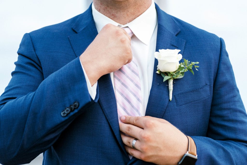 Tampa groom fixing his tie wearing a navy tuxedo with a white flower bouttoniere