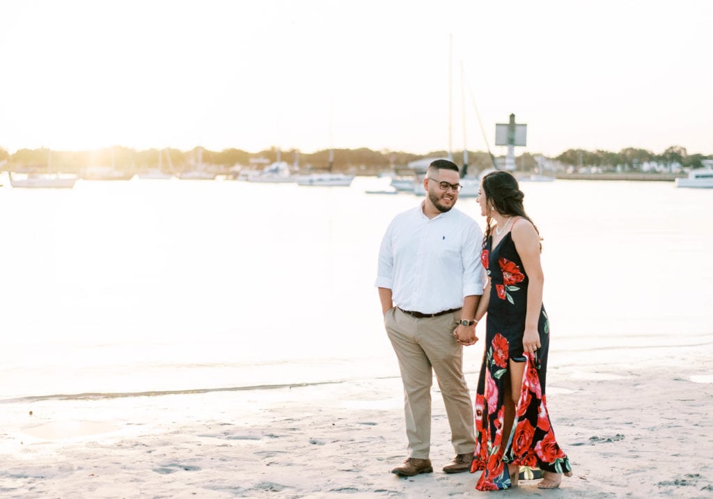 Davis Island Engagement Photos at sunset couple holding hands walking on the beach boats in the background