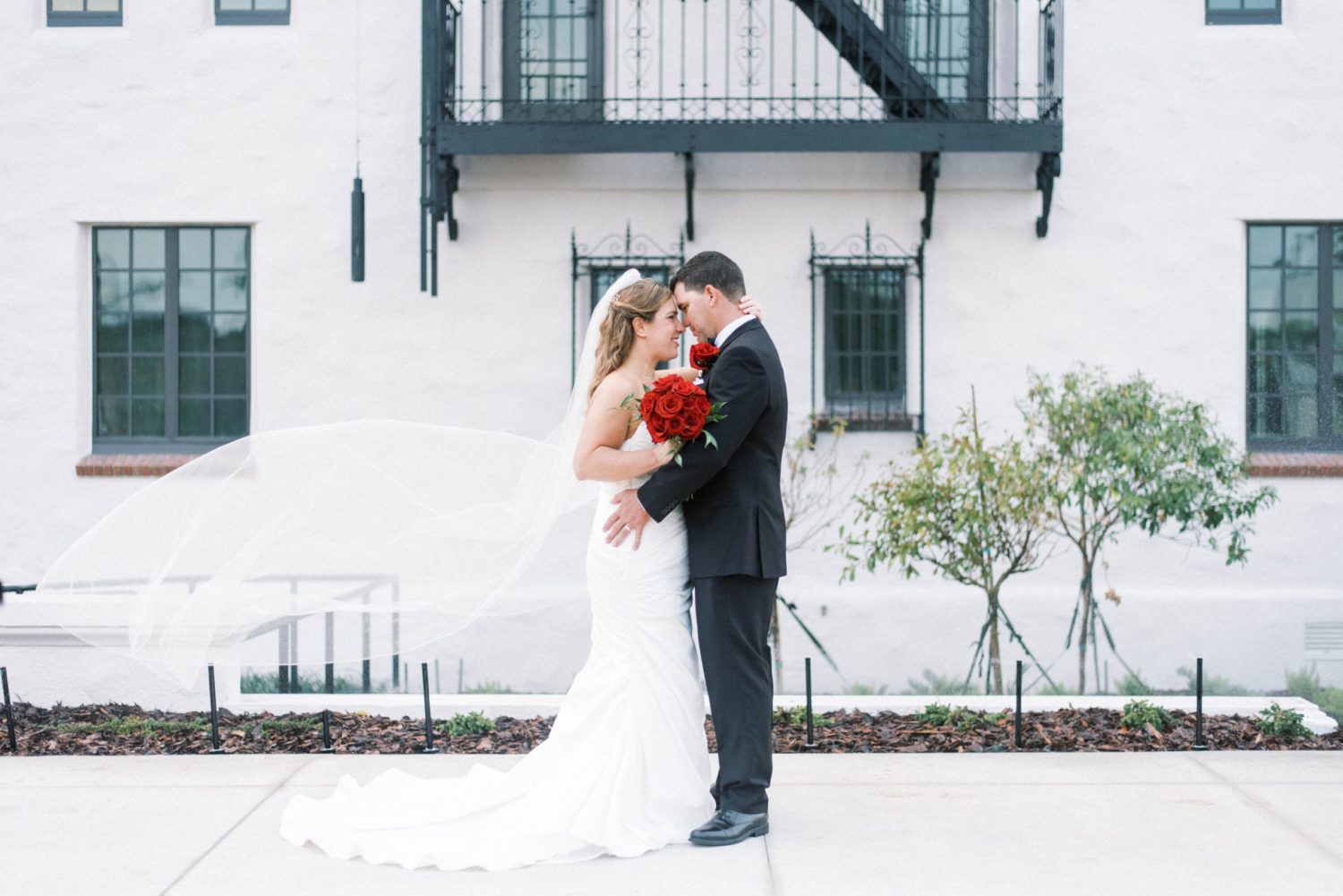 Hyatt Regency Sarasota Wedding in Classic White Black and Red Wedding Color Palette Photo of Bride and Groom embracing each other long veil in the air