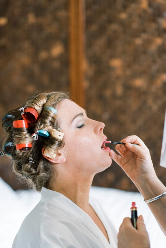 Bride in rollers getting her lipstick on for her wedding