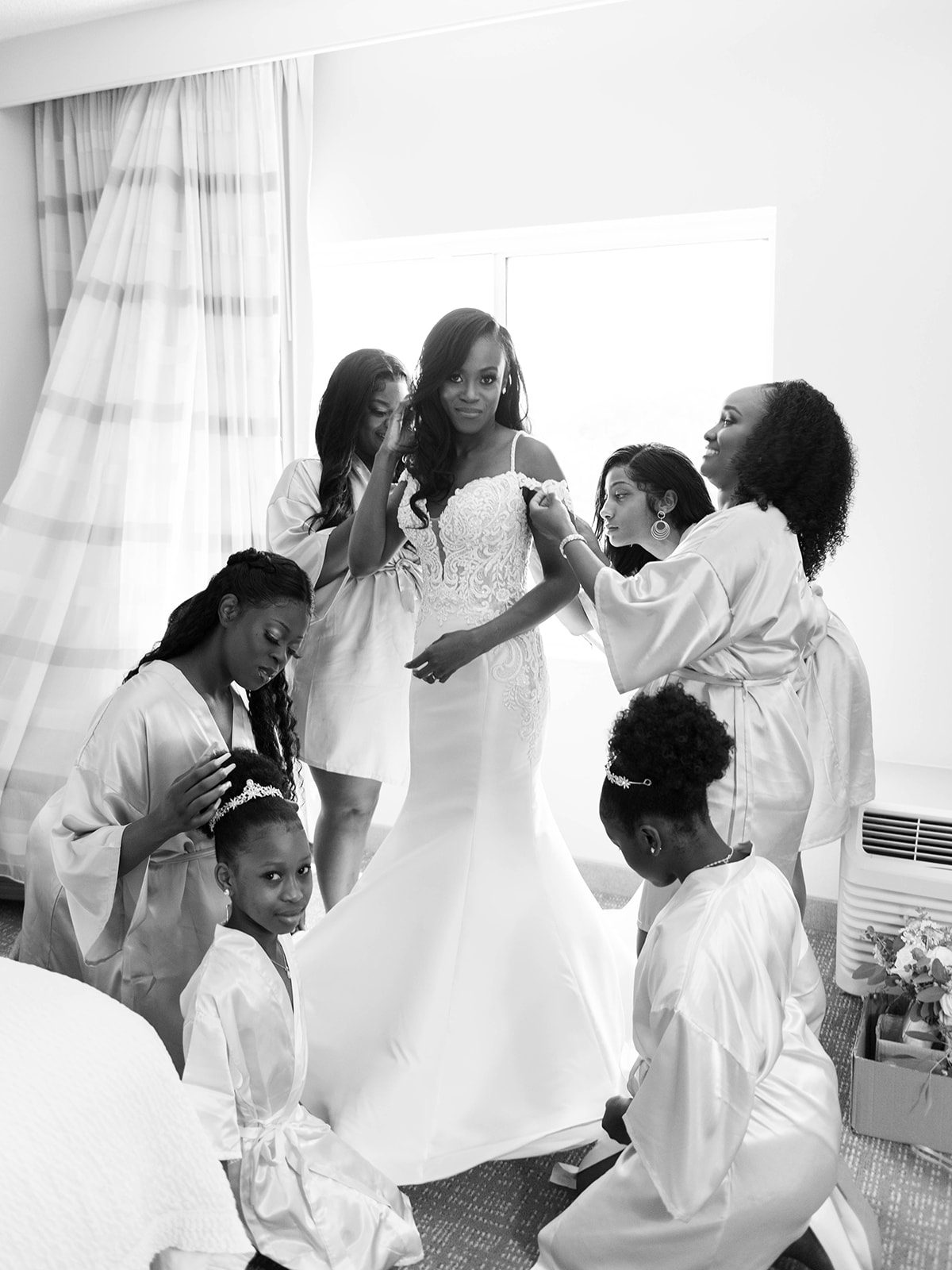 black and white photo of the bride getting ready before her wedding ceremony in Tampa FLorida and all of her bridesmaids and flow girls are gathered around her helping her get ready