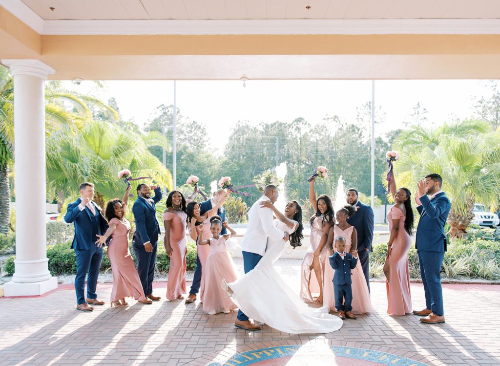 groom dipping his bride on their Florida wedding day as she laughs and the wedding party cheers them on at their Bayanihan Arts and Events Center wedding venue