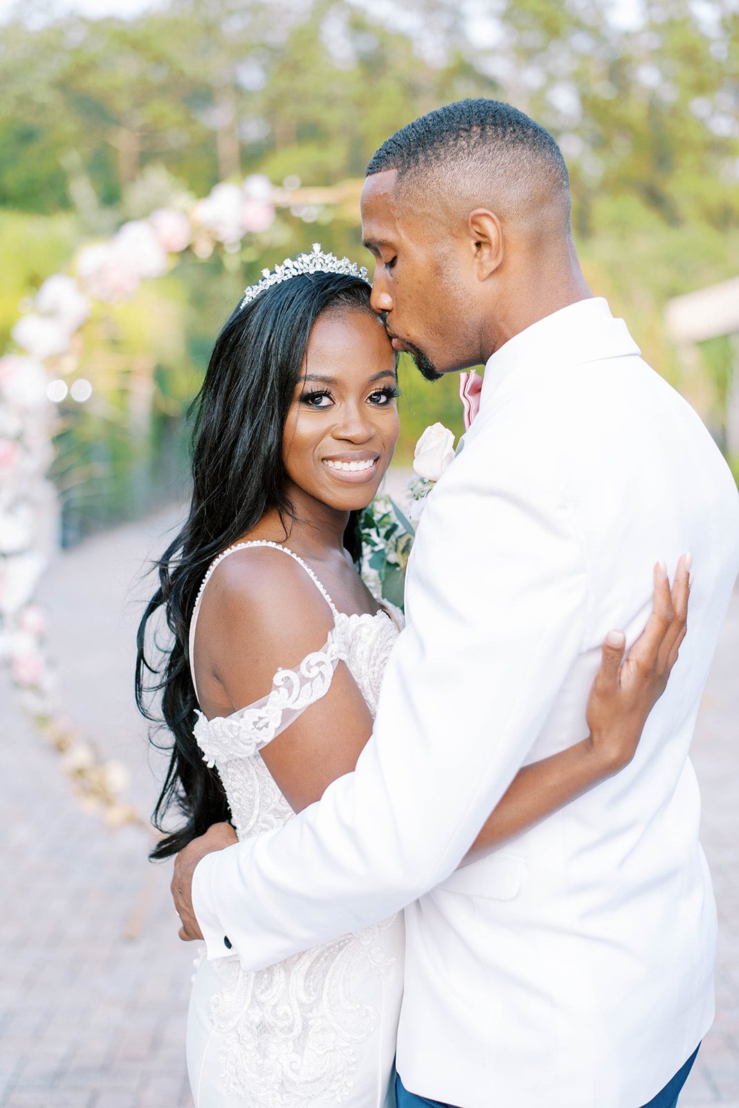 groom kissing brides forehead as she holds him and smiles at the camera