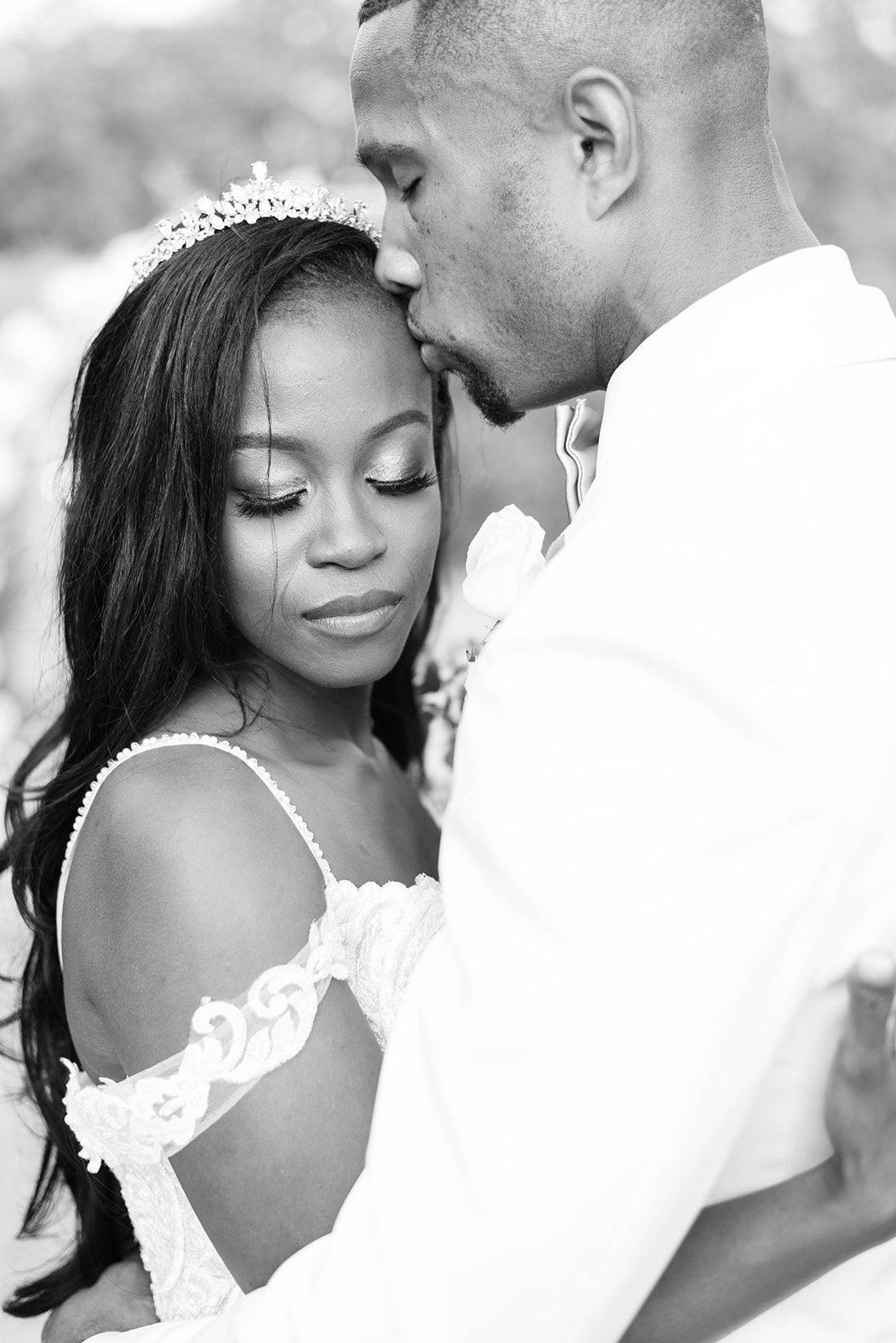 black and white photo of groom kissing womans forehead as she holds him close