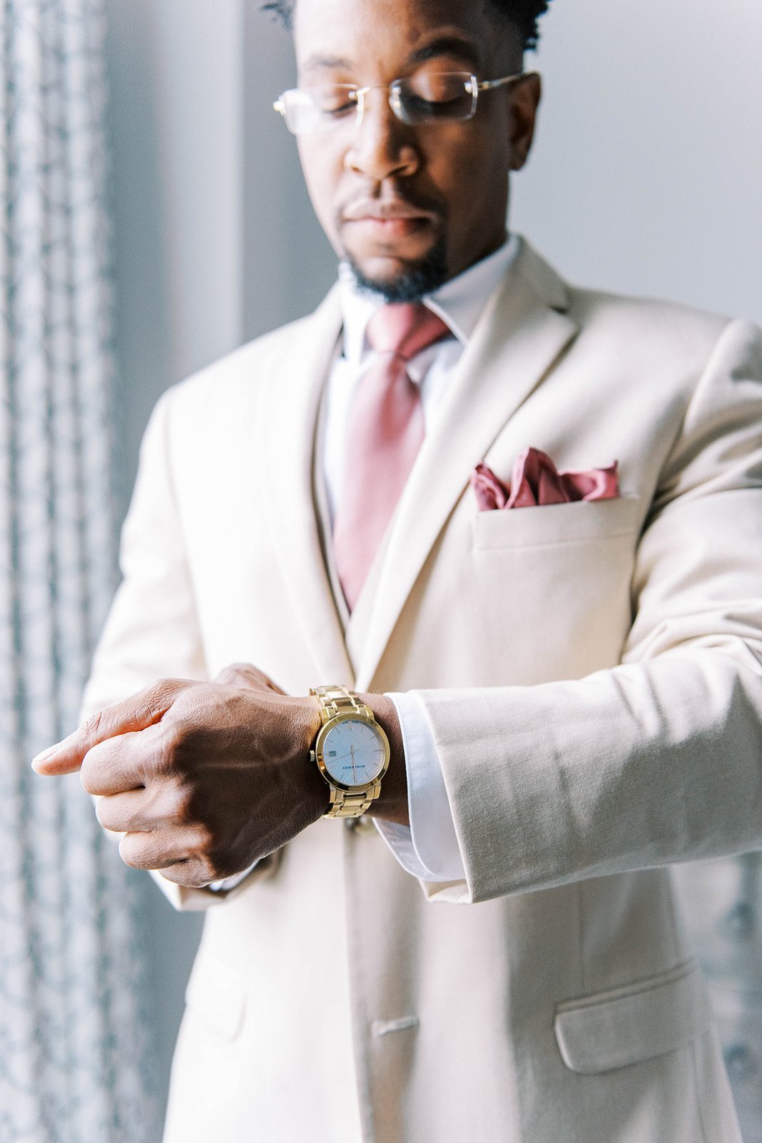 groom in a beige suit fixes his cuffs in front of a window before his Tampa wedding ceremony captured by Tampa Bay weddin gphotographers