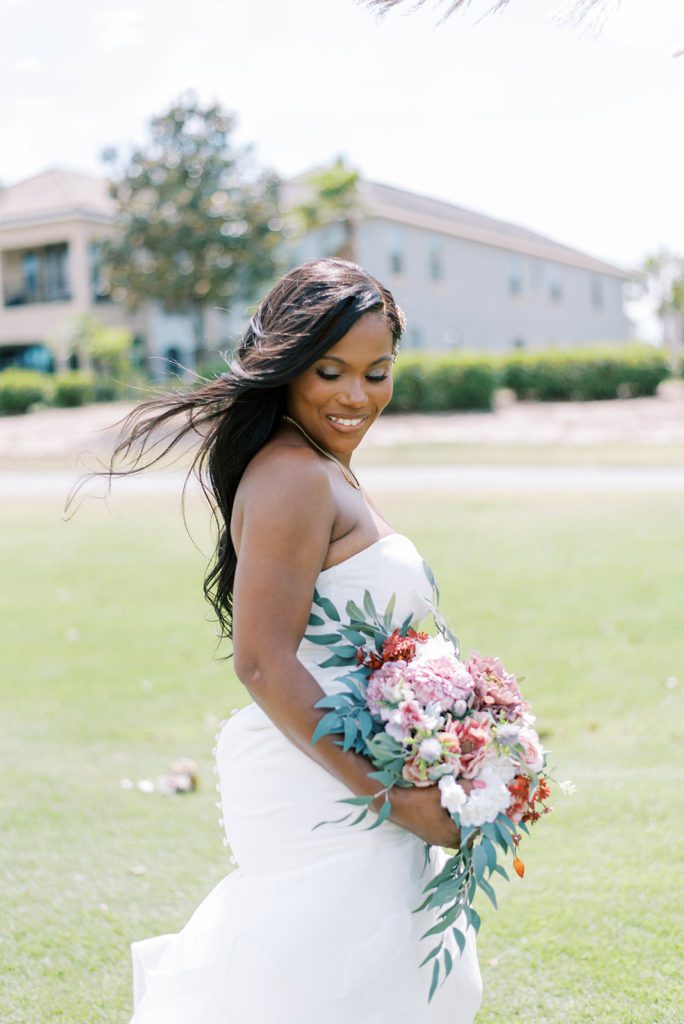 bride looking down at the ground as she holds a stunning green and blush wedding bouquet as the wind blows her hair off of her shoulder