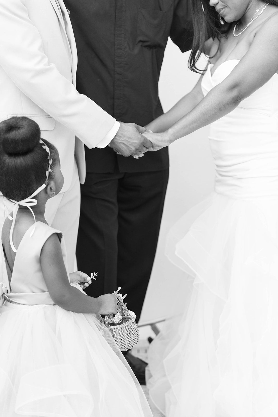 black and white image of bride and groom holding hands during there wedding ceremony and their daughter who is a flower girl is looking up at them