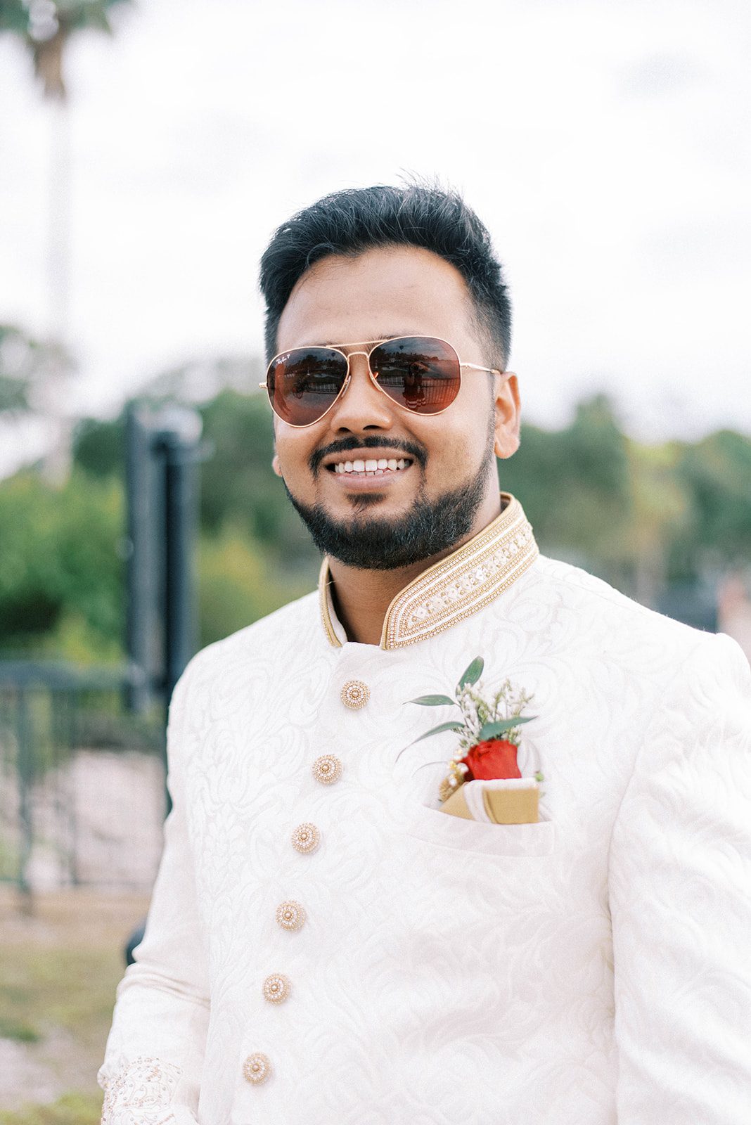 Indian groom wearing a traditionally white wedding suit with a red rose on his pocket