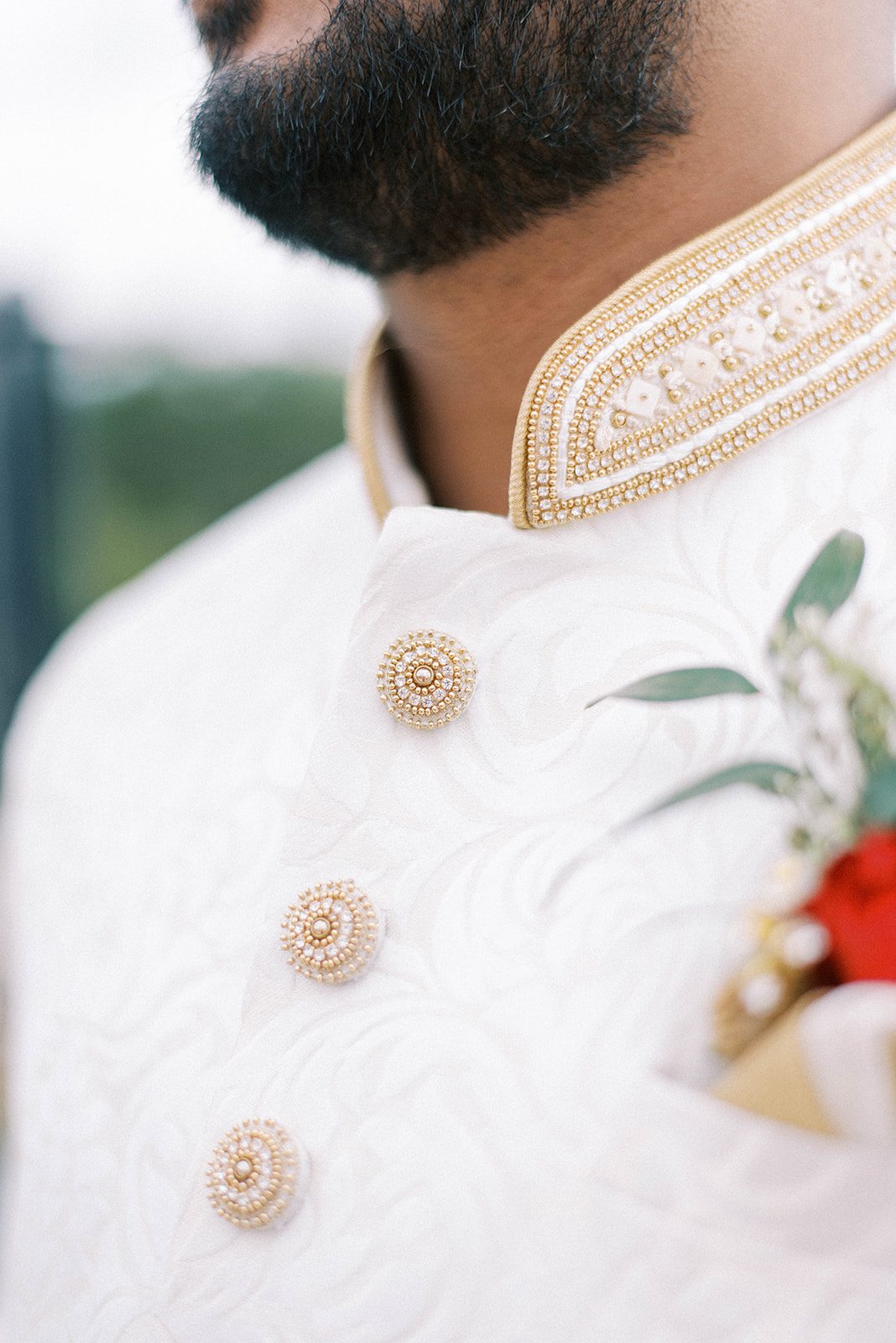 close up detail shot of Indian wedding outfit for the groom in a white suit with beaded buttons and collar