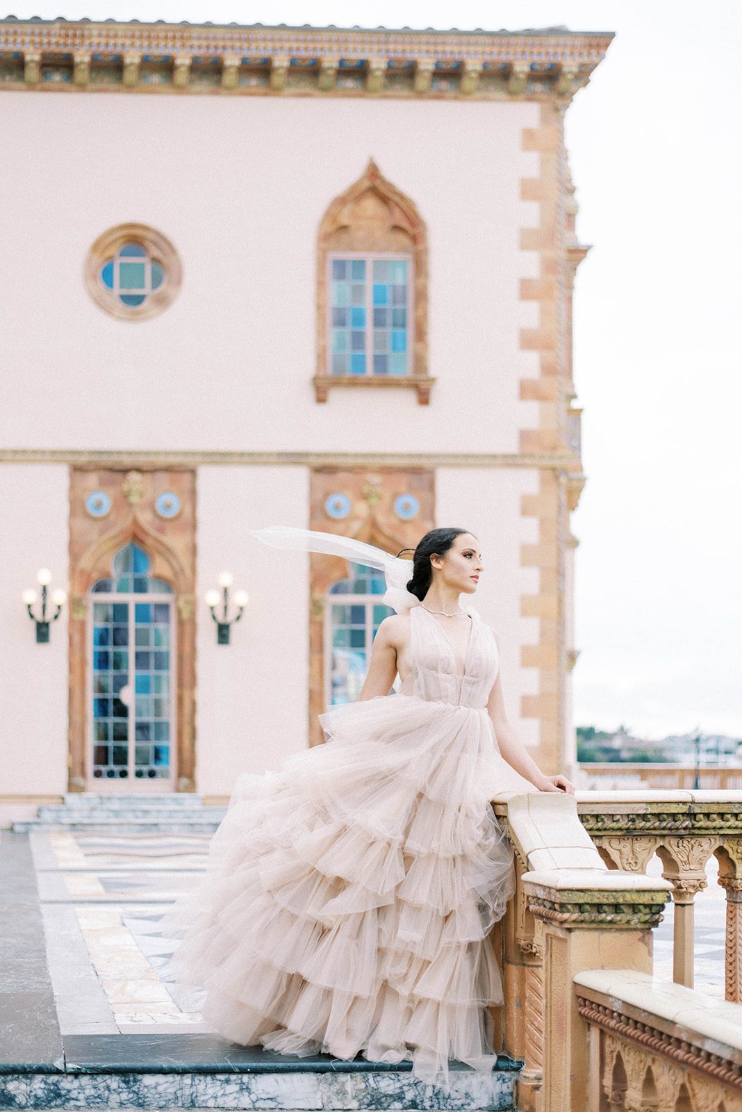 bride at the Pink Hotel near Tampa Florida looking off the deck into the ocean as her ruffle light blush wedding dress blows in the wind