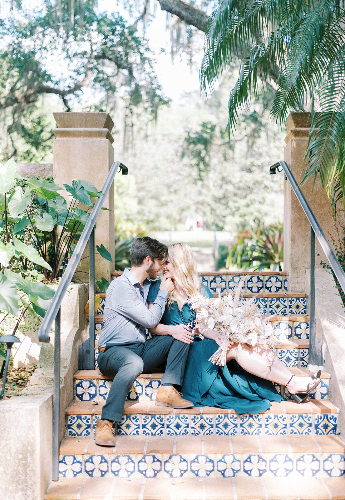 engaged couple sit on stairs with spanish influencced tiles and kiss for their engagement photos in Bok Tower Gardens in Tampa Florida