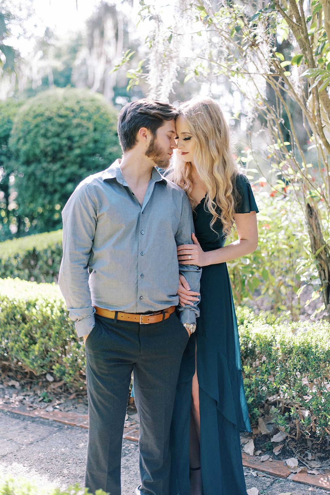 Bok Tower Gardens engagement photos in Tampa Florida with man and woman embracing each other while wearing blues and emerald greens