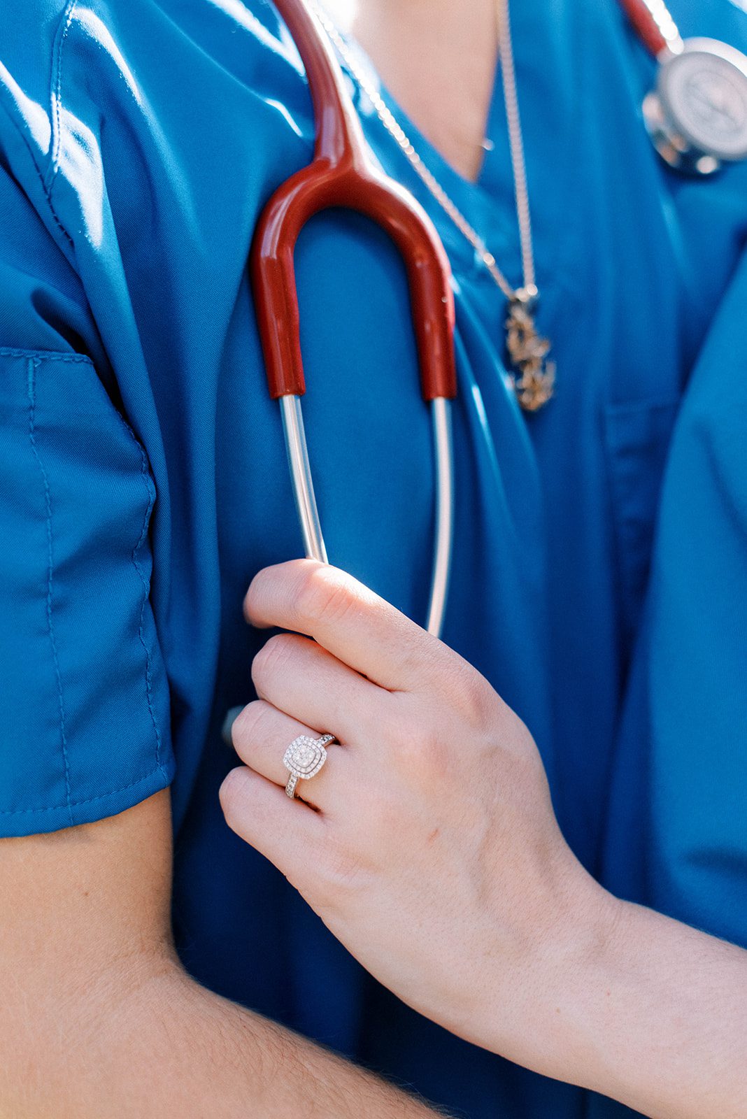 man and woman wearing scrubs for their engagement session with woman holding the mans stethoscope for a detail shot of her engagement ring