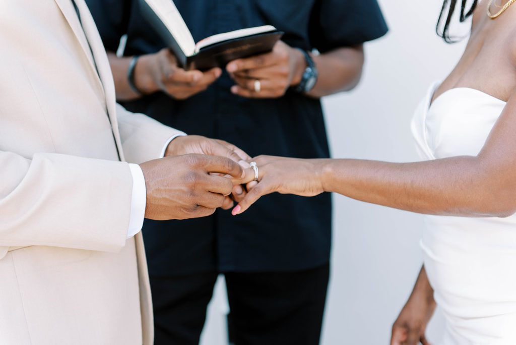 airbnb micro wedding groom putting ring on bride with officiant in the back