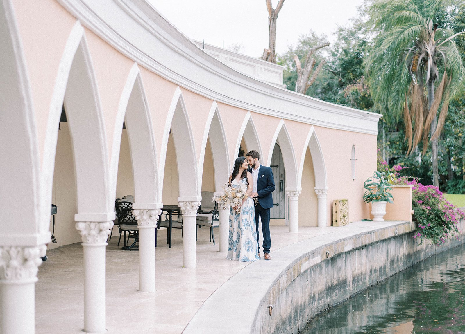 The Mirasol engagement photos in Tampa FLorida with man holding woman and leaning into her next to a water feature and beautiful hallway for arches outside