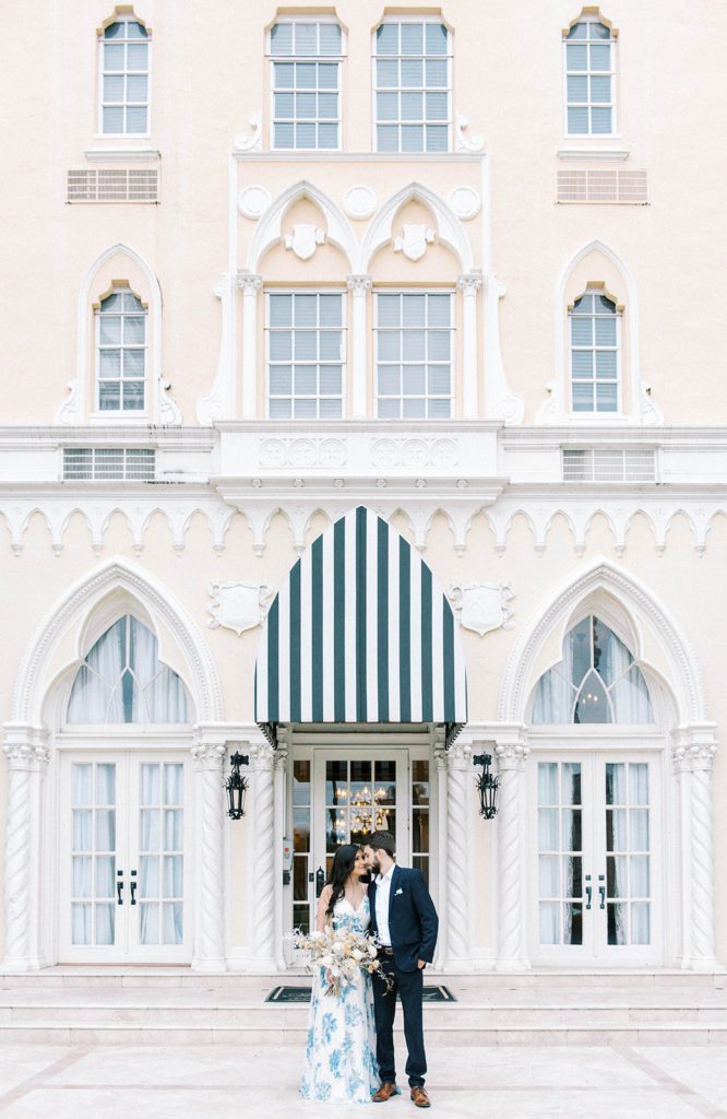 The Mirasol engagement photos featuring multiple stories of the building with tall three point arched windows and bright walls, with man and woman standing together and leaning into one another and smiling elegantly 