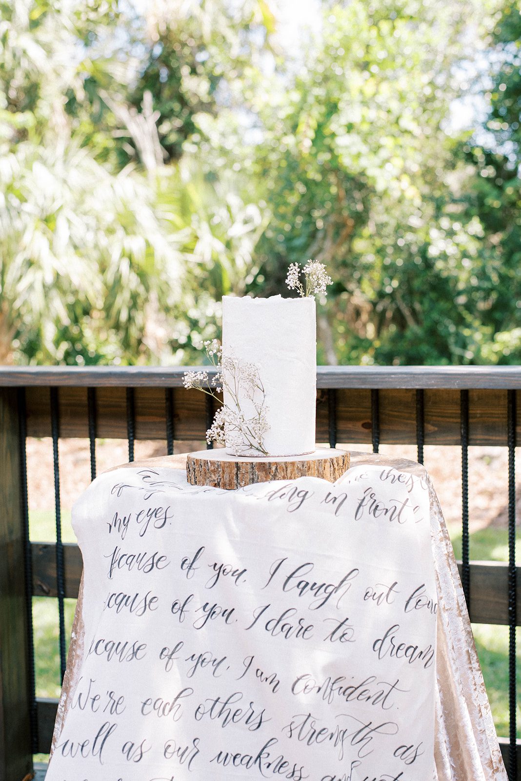 wedding cake on a wooden stand that is sitting on a a table with a personalized tapestry