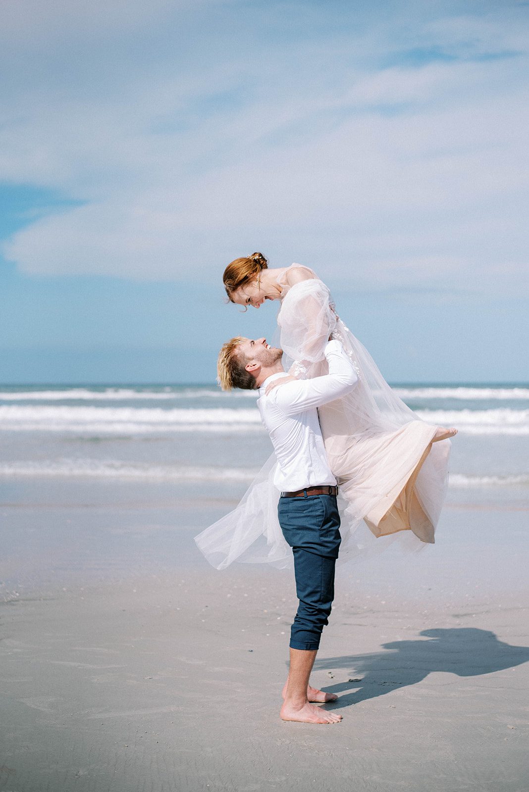 Minimalist Styled Wedding with bride and groom at New Smyrna Beach in Florida on their wedding day with groom picking up bride and spinning her around as she smiles and laughs