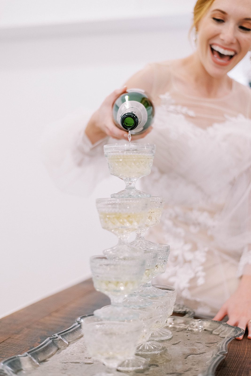 bride smiling and laughing as she pours champagne down a tower of champagne glasses