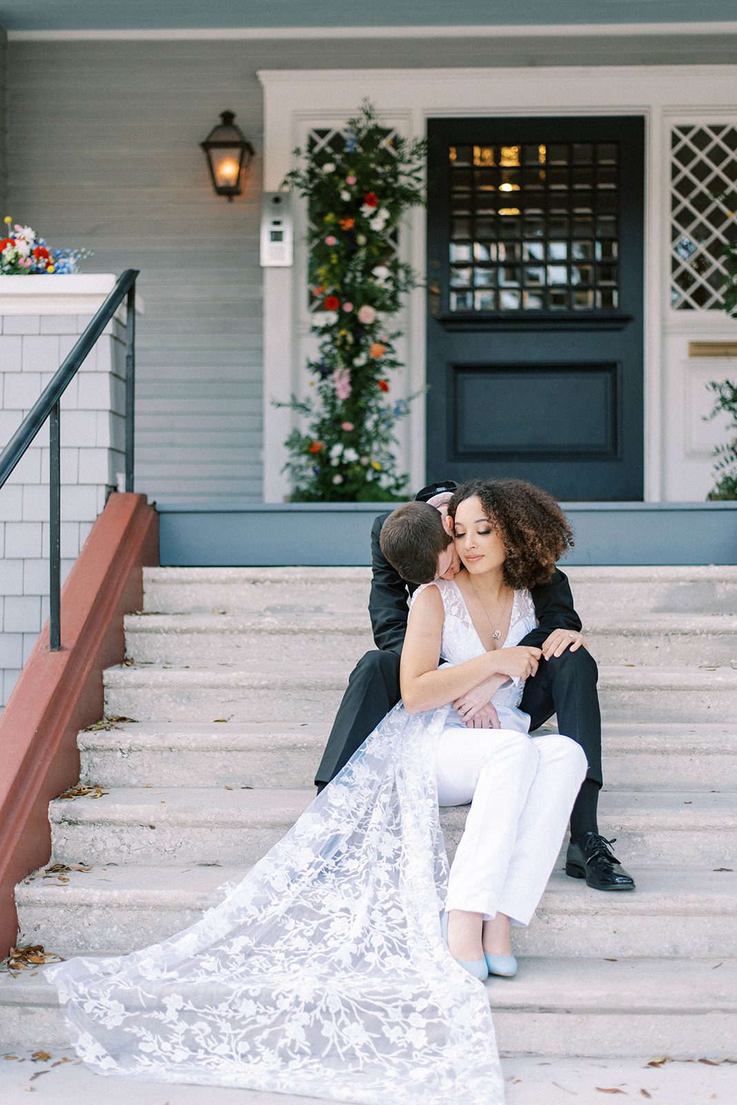 The Orlo wedding in Tampa Florida with bride and groom sitting on the front porch steps as the groom kisses his brides shoulder and she smiles slightly towards him