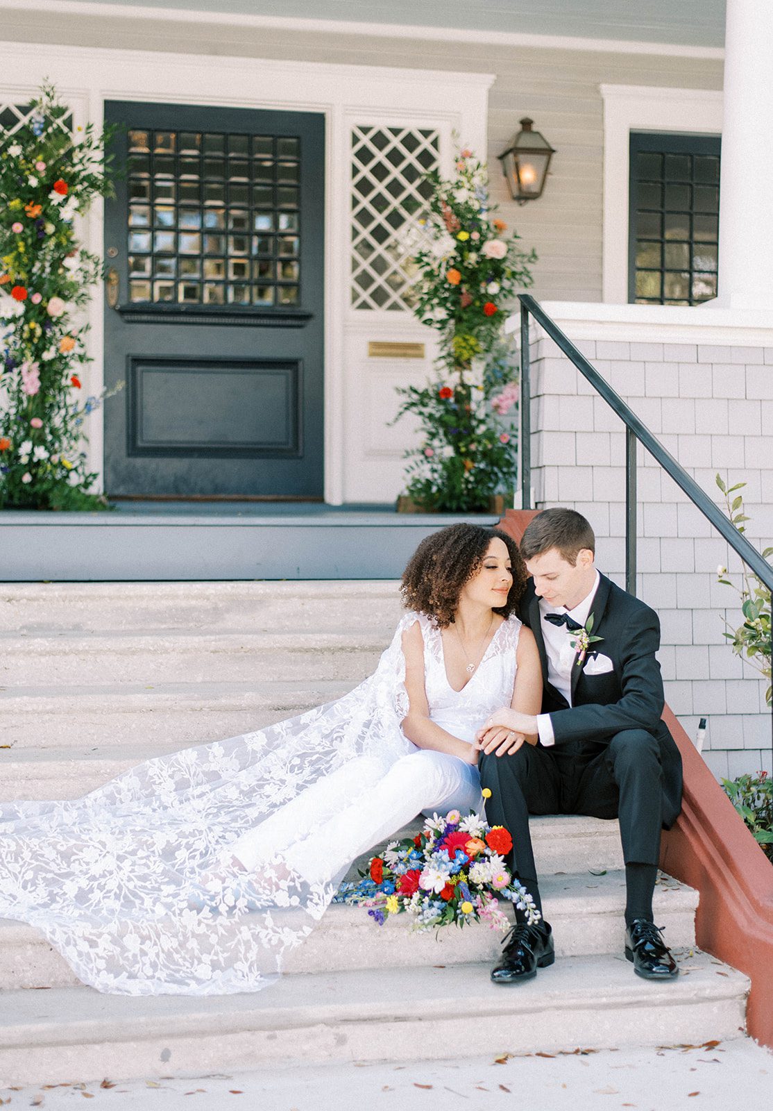 wedding day couple sitting on the front stairs of the Orlo in Tampa Florida embracing each other with gorgeous florals decorating the door behind them