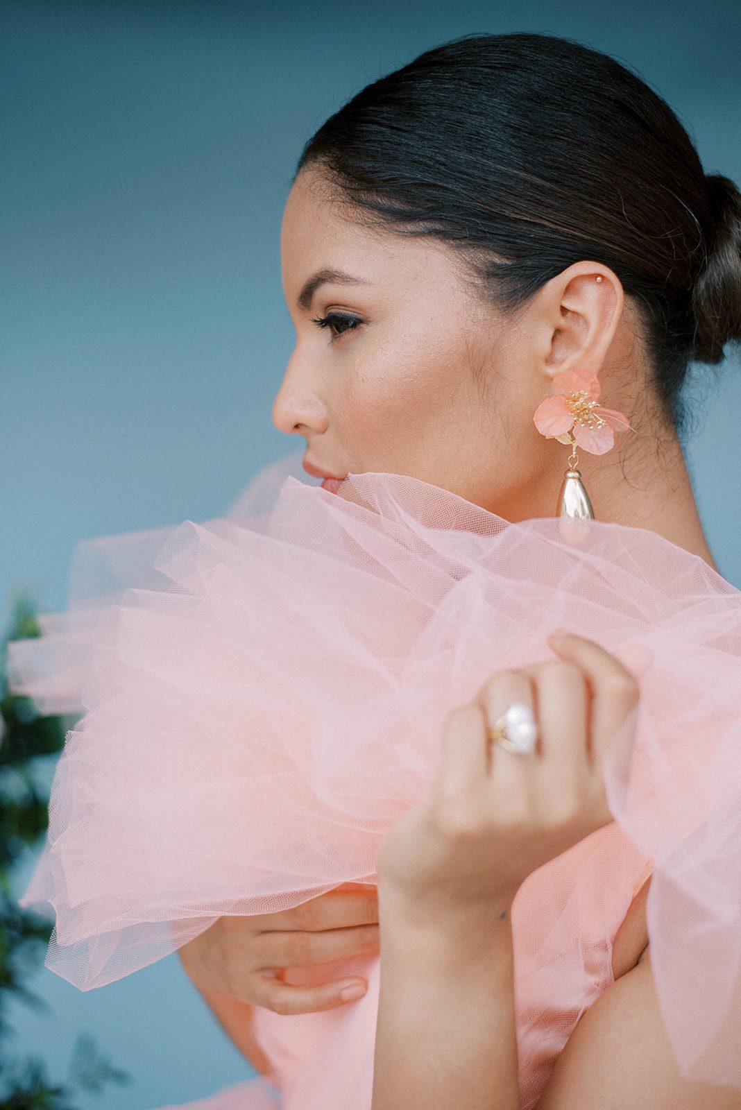 detail shot of a bride in a pink tulle gown facing to the side as she holds her hand up to the camera