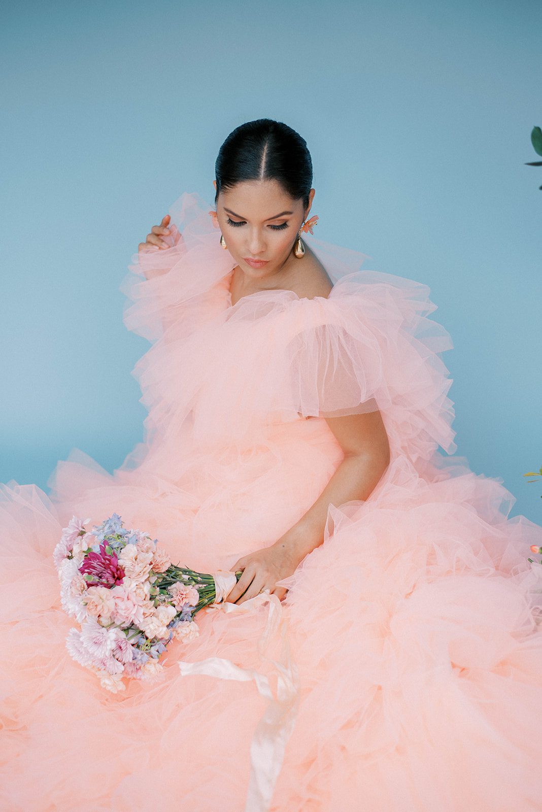 bride in a large pink gown sitting with a bouquet of florals on her lap