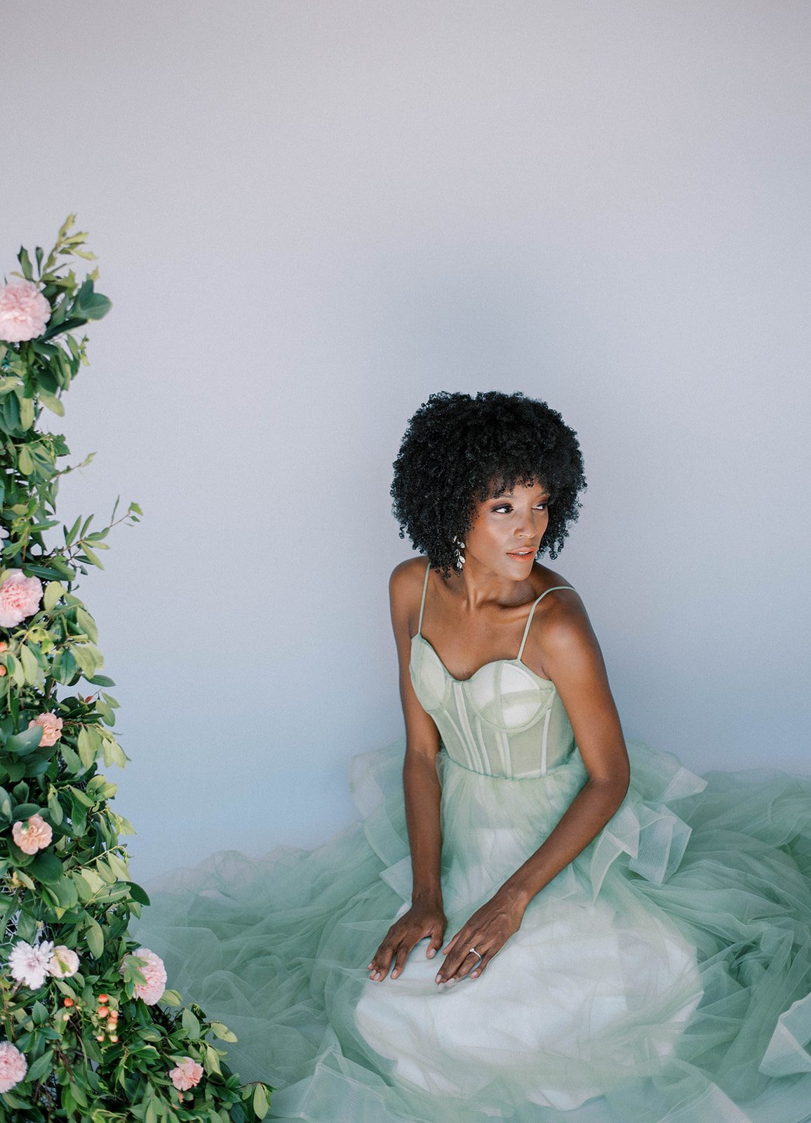 bride sits in pale green wedding dress by pink and green floral display for Tampa wedding