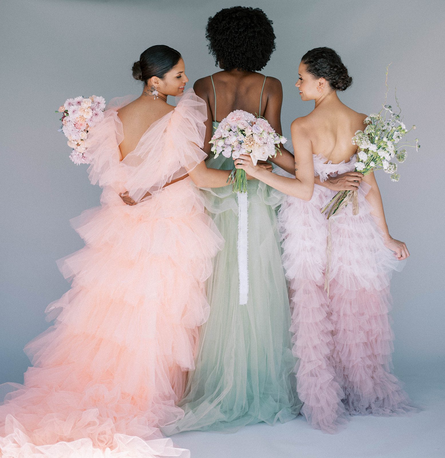 three bride standning together and facing away from the camera to show off the back of their dresses, all three are wearing different colored wedding dresses for a Tampa Florida colorful bridal fashion wedding shoot