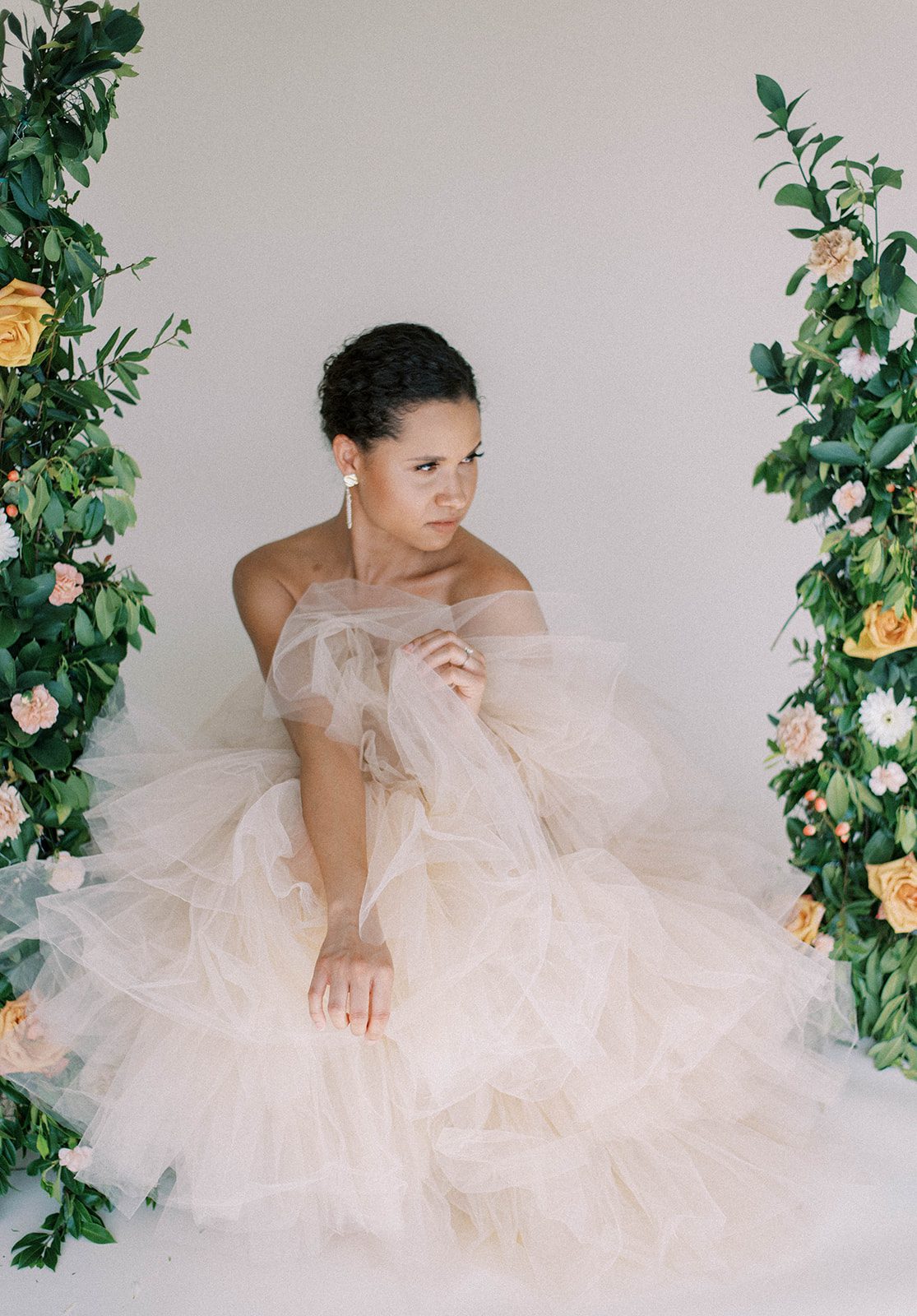 bride in a puffy cream wedding dress sits in the middle of the floral with florals surrounding her