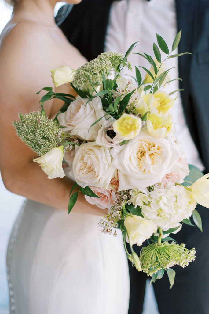 bride holding a white and yellow wedding day bridal bouquet as she holds onto her groom with her other arm