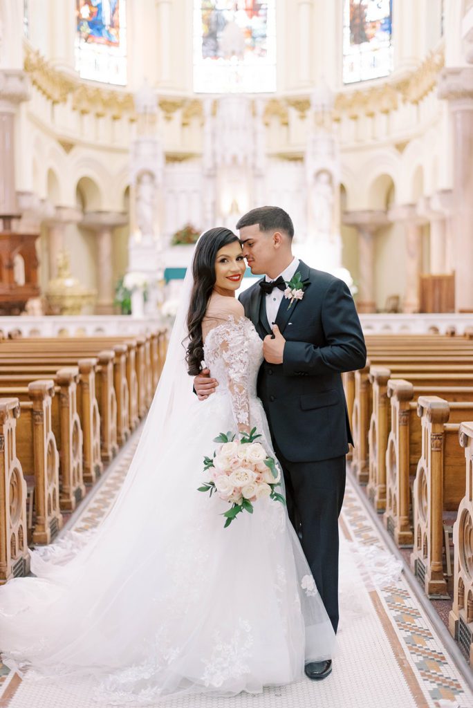 wedding planning, bride and groom in a gorgeous stain glass chapel in Florida with the groom holding his bride closely as she looks over her shoulder and smiles at the camera