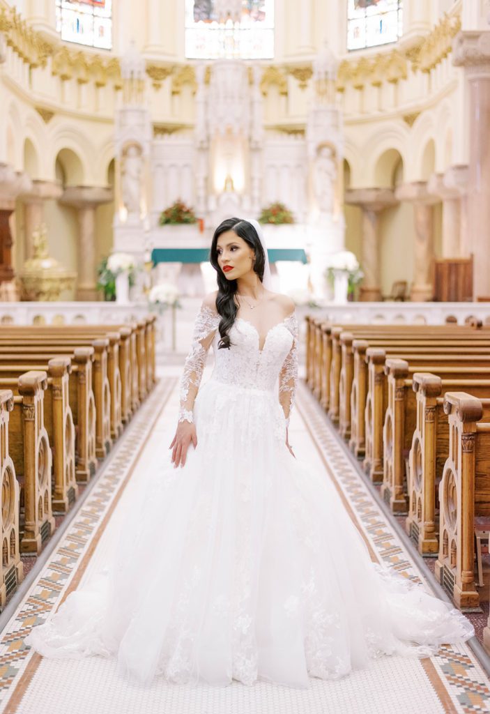 dark haired bride with a stunning tulle and lace gown standing in a stain glass cathedral in Tampa Florida