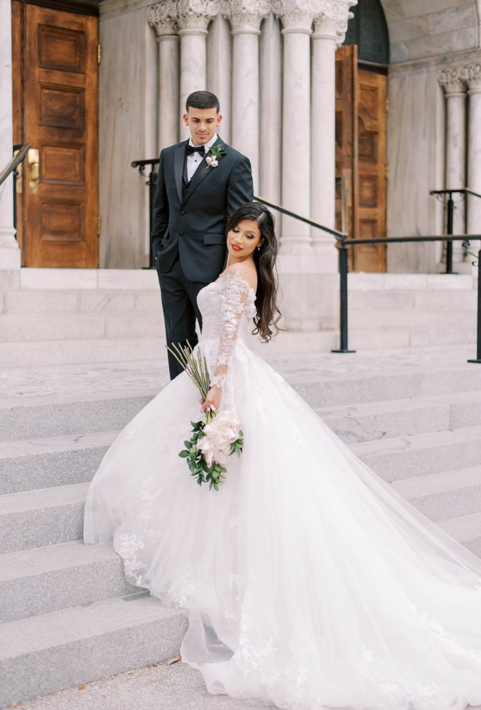 Tampa wedding photography with bride and groom walking up the church's outside stairs together as the bride looks back over her shoulder romantically