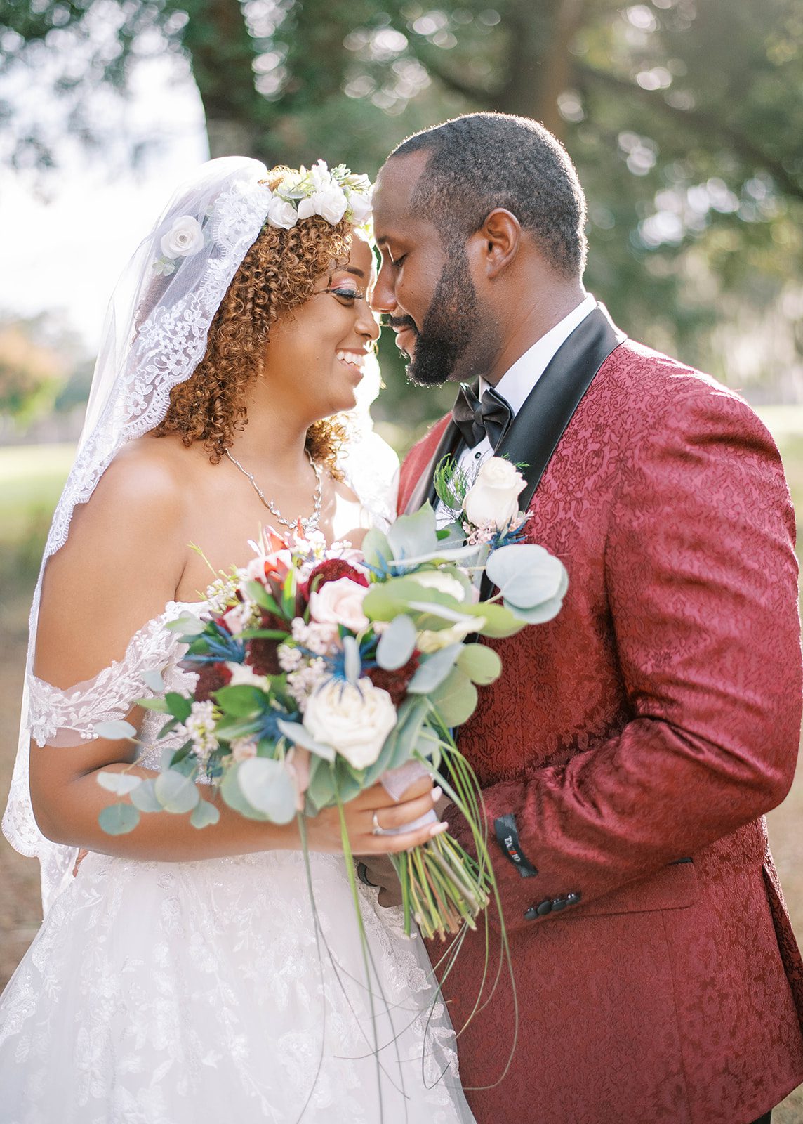 bride and groom embracing on their wedding day with bride in a stunning off the shoulder wedding dress, and groom wearing a dark red burgundy suit coat in Tampa Florida