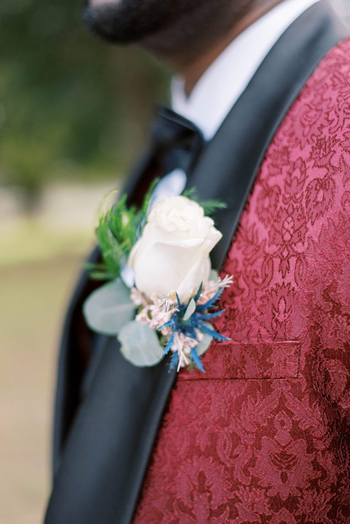 close up shot of grooms white rose boutonniere against his maroon suit on her wedding day in Tampa Florida