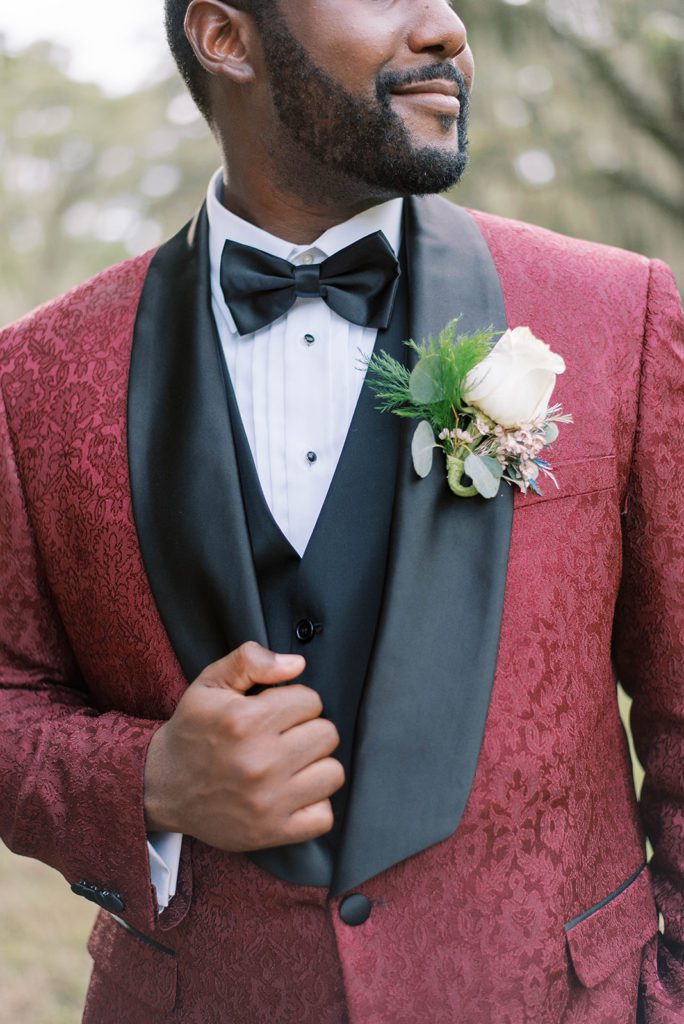 african american groom posing in a burgundy suit and looking off to the side on his wedding day in Tampa Florida