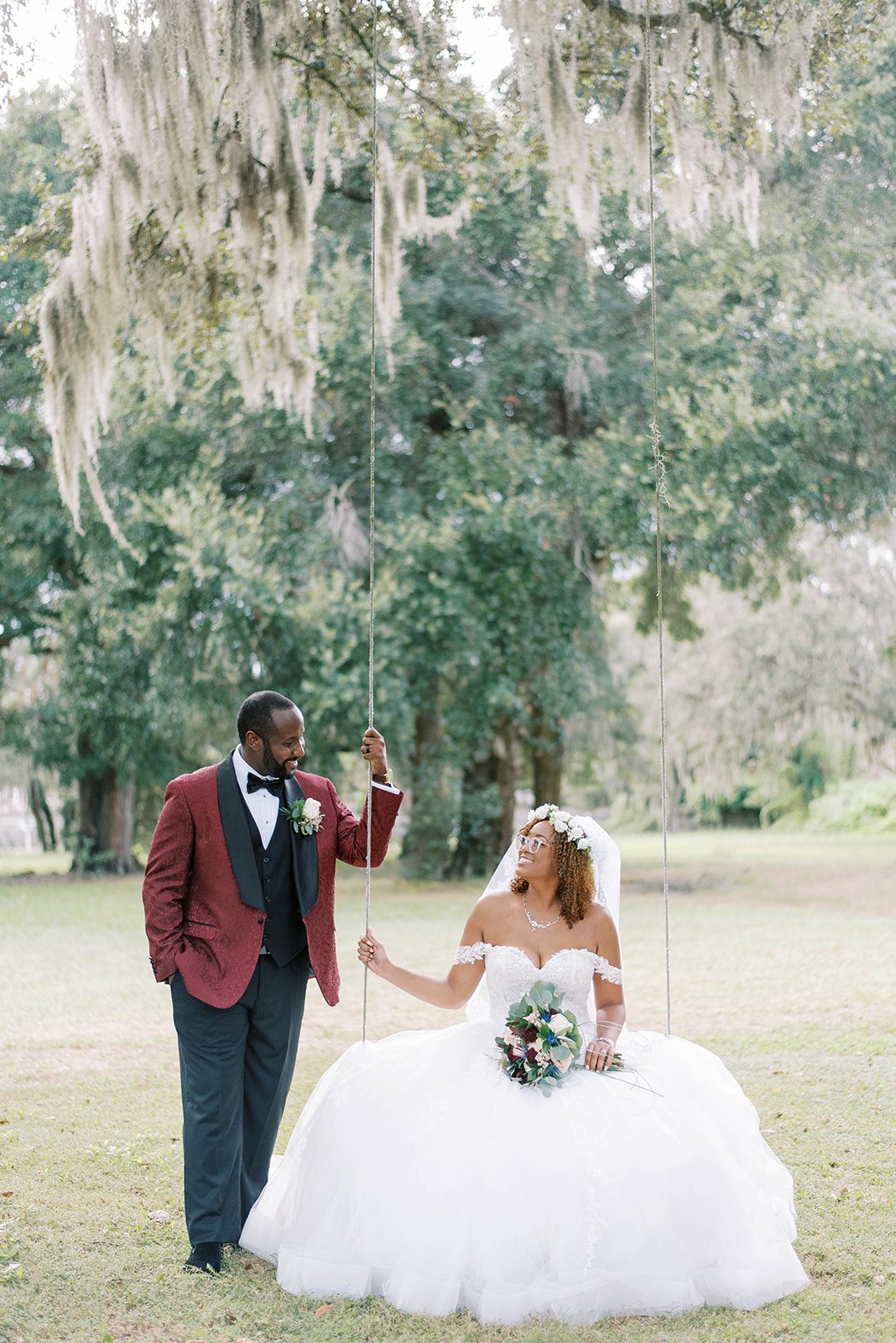 bride sitting on a wooden swing that is attached to a large tree in Tampa FLorida as she looks up to her groom who is holding onto the swing and smiling down at his bride, hire a wedding planner