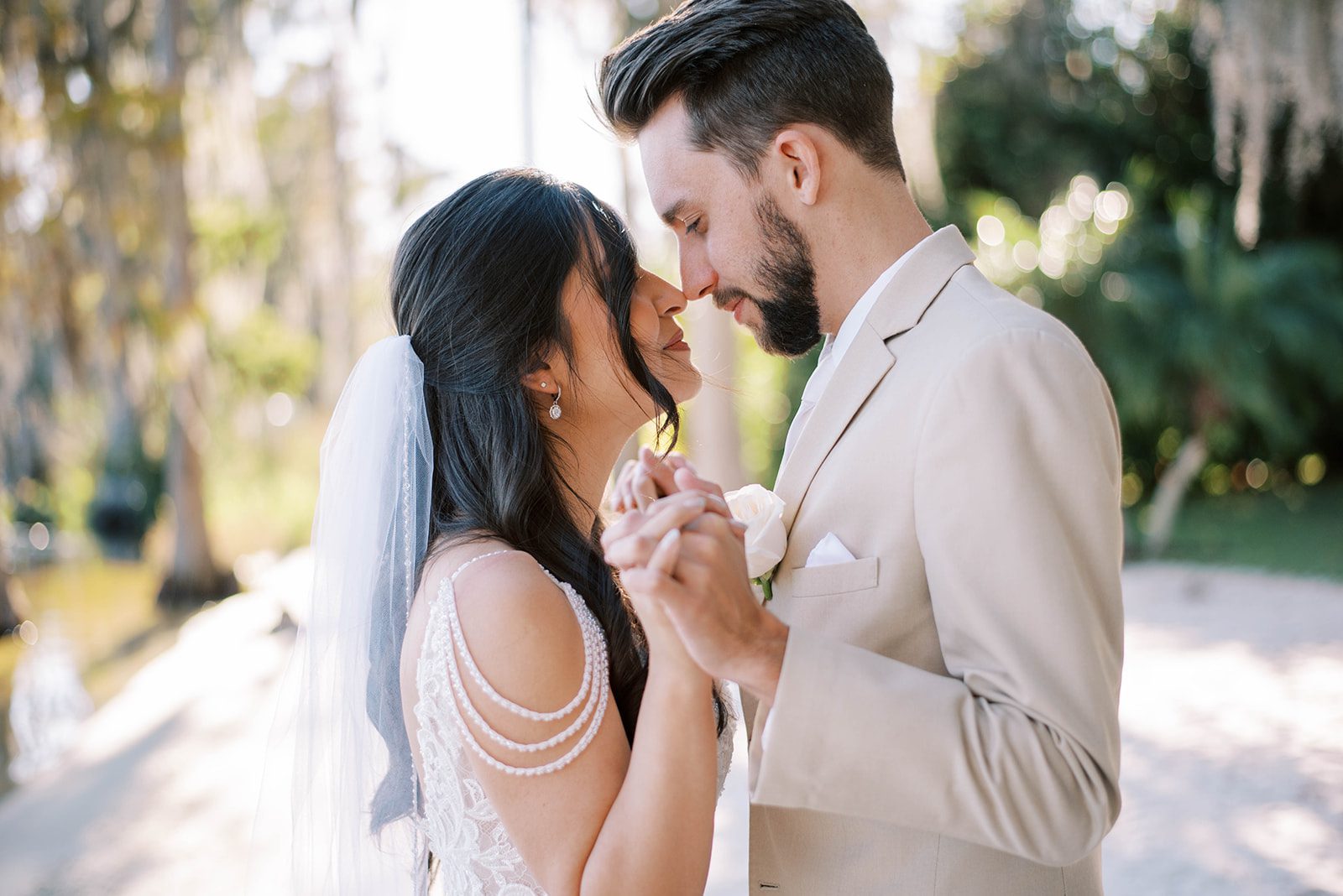 Wedding Vendors Search Etiquette, bride in a stunning 20s era inspired wedding gown holds hands with her groom who is wearing a tan suit as their noses touch and they gently smile at one another in Tampa Wedding
