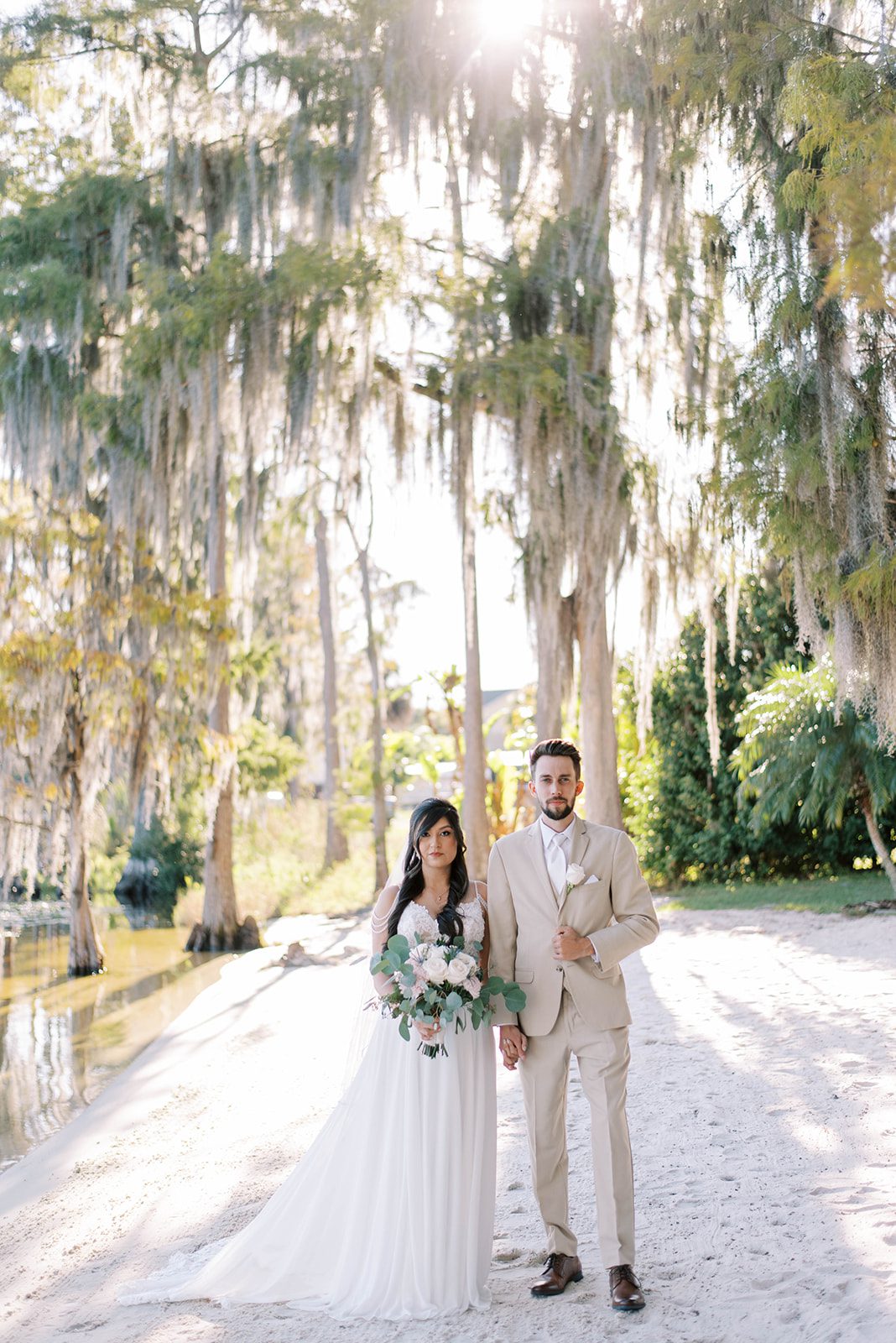 bride and groom standing together and holding hands on their wedding day with bride holding a white florals bouquet and the groom holding his suit coat for a very regal wedding portrait, Wedding Vendors Search Etiquette