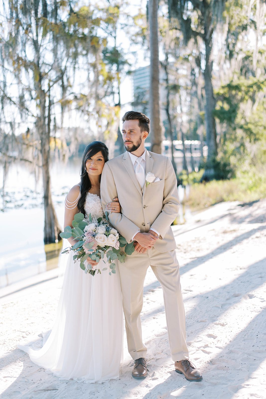 bride and groom standing together for their Florida outdoor wedding with the bride holding the groom by his arm as they both look off to the distance