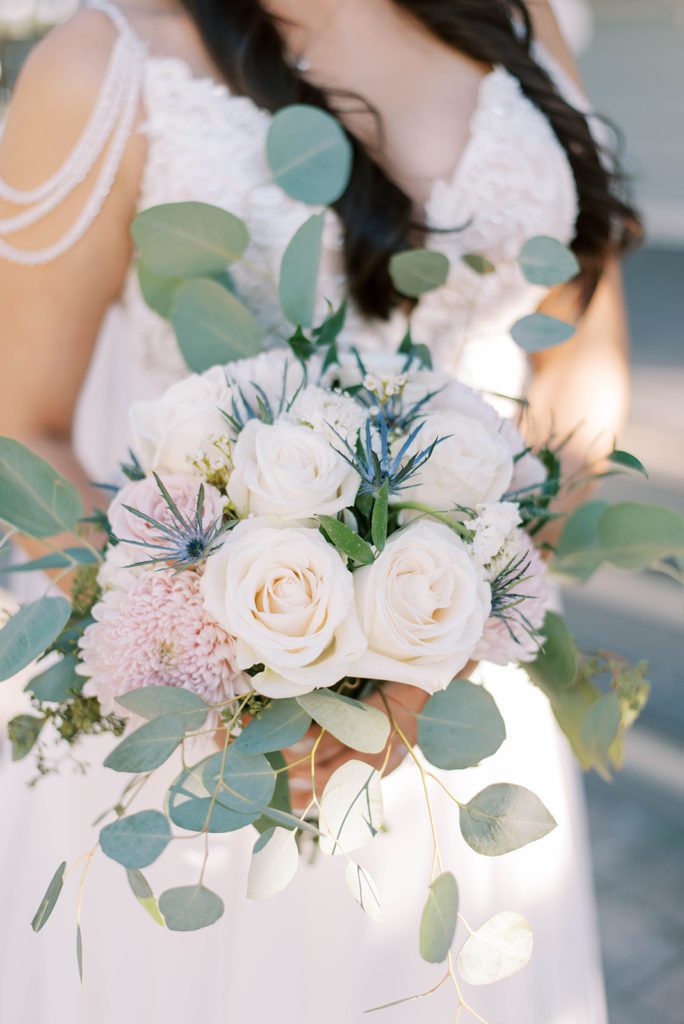 detail shot of bridal florals with bride holding her wedding bouquet that is filled with white roses and eucalyptus leaves